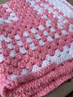 a pink and white crocheted blanket sitting on top of a wooden table