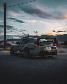 a grey sports car parked on the side of the road at dusk with clouds in the background