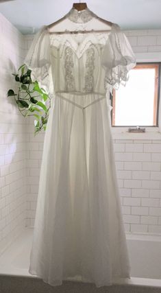 a white dress hanging on a rack in a bathroom next to a potted plant