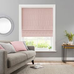 a living room with a couch, table and window covered in pink roman blind shades