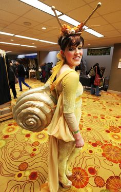 a woman in costume standing on a carpet with a snail shell and two large swords