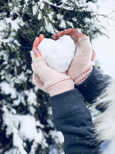 a person holding a heart shaped snowball in their hands while standing next to a tree