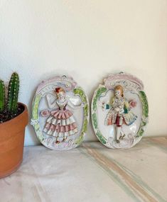 two decorative plates sitting on top of a table next to a cactus in a pot