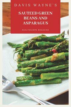 a white plate topped with asparagus on top of a wooden table next to a fork