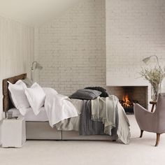 a bedroom with a bed, chair and fire place in the corner is white brick walls