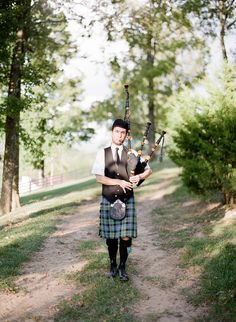 a man in a kilt playing bagpipes on a dirt path near trees