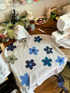 a white sweatshirt with blue flowers on it sitting on top of a table next to other crafting supplies