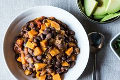 a white bowl filled with beans and vegetables next to an avocado wedges