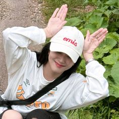 a woman sitting on the ground wearing a hat and holding her hands up in front of her head