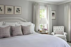 a white bed sitting in a bedroom next to a window covered in curtains and pillows