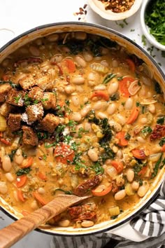 a pot filled with stew and vegetables on top of a white tablecloth next to bowls of food