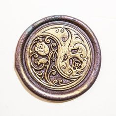 a metal button with an intricate design on the front and back side, sitting on a white surface