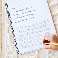 a child's hand holding a pencil and writing on a notebook with cursive writing