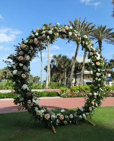 a wedding arch with flowers and greenery on the grass in front of palm trees