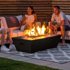 two people sitting on couches in front of a fire pit with lit candles and wine glasses