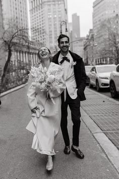 a man and woman are walking down the street in front of some tall buildings while holding flowers