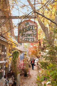 a woman walking down a path in front of a flower shop with an american flag hanging from the roof