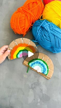 someone is holding yarn in front of some balls of yarn and a paper plate with a rainbow on it