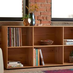 a book shelf with books and magazines on it in front of a brick wall next to a white chair