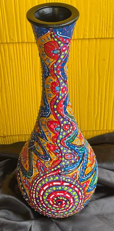 a colorful vase sitting on top of a black cloth covered table next to a yellow wall