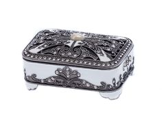 a white and black jewelry box with an ornate design on the lid, sitting on a white surface