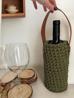 a person holding a wine bottle in a basket next to some wood slices and glasses