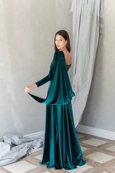 a woman standing in front of a curtain wearing a green velvet dress with long sleeves