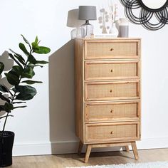 a wooden dresser sitting next to a mirror on top of a white wall in front of a potted plant