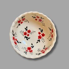 a white bowl with red flowers and black dots on the rim is sitting on a gray surface