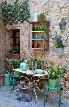 an outdoor table and chairs in front of a stone building with potted plants on it