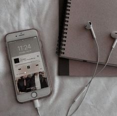 an iphone and headphones are laying on a bed next to a notebook with ear buds