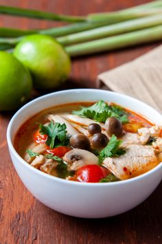 a white bowl filled with soup next to green onions and limes on a wooden table