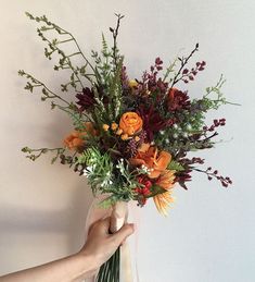 a person holding a bouquet of flowers in front of a white wall with red, orange and yellow flowers