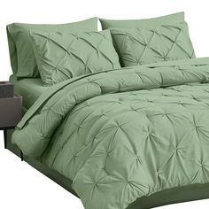 a bed with green comforters and pillows on it's side, in front of a night stand