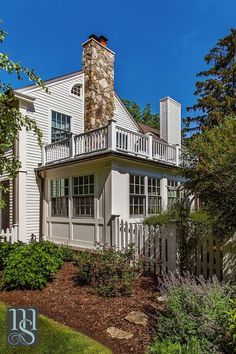 a white house with a stone chimney on the top floor and two story balcony above it