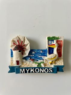 a ceramic sign that says mykonos with a lighthouse and beach in the background