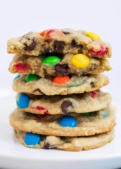 a stack of cookies with m & m's and chocolate chips on top in front of a white plate