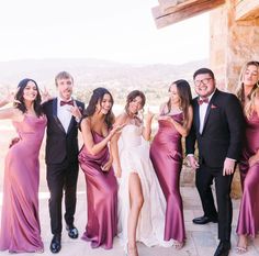 a group of people standing next to each other in front of a stone wall wearing purple dresses