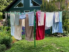 clothes hanging out to dry in front of a blue house with green grass and flowers