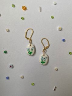 two earrings with flowers on them are hanging from gold earwires against a white background