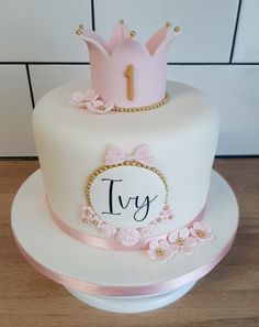 a white cake with pink frosting and a crown on top that says 1yr