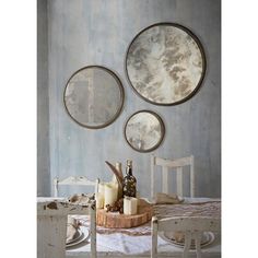 three round mirrors hanging on the wall above a dining table with candles and cheeses