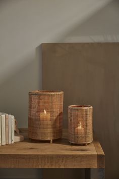 two wicker candle holders sitting on top of a wooden table next to some books