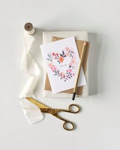 a pair of gold scissors next to a card and some tape on a white surface