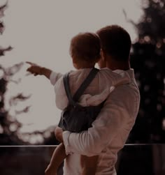 a man holding a child in his arms and pointing to something on the other side