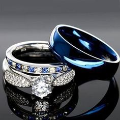 two wedding rings with blue and white diamonds on black reflective surface in front of dark background