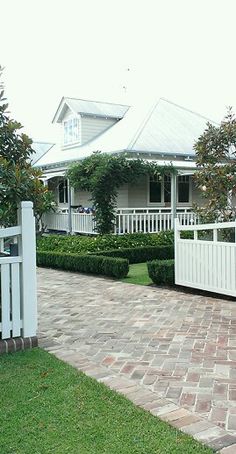 a white picket fence in front of a house with hedges on the sides and trees around it