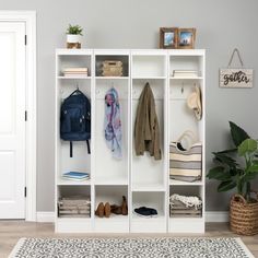 a white bookcase filled with clothes next to a rug and potted plant on top of a hard wood floor