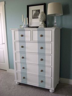 a white dresser sitting in a bedroom next to a lamp and pictures on the wall