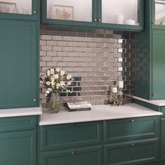 a kitchen with green cabinets, white counter tops and flowers in a vase on the island